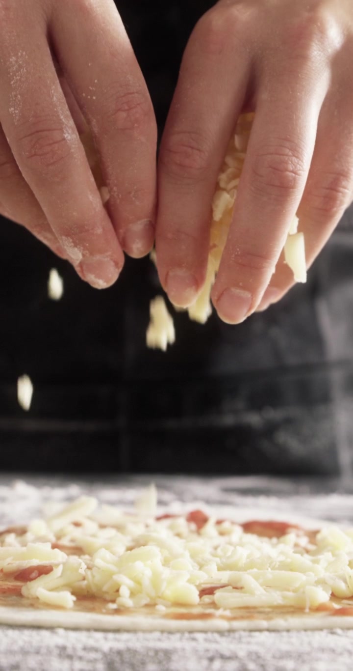 Chef che sparge formaggio grattugiato sull'impasto della pizza