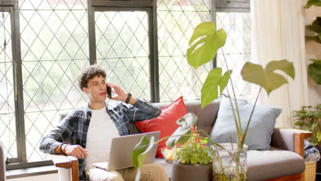 Biracial-man-working-from-home-using-laptop-and-talking-on-smartphone,-slow-motion