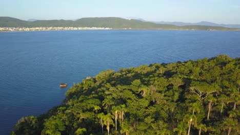 Toma-Aérea-Del-Carro-Volando-Sobre-Una-Colina-Cubierta-De-Vegetación-Y-El-Mar-Y-La-Ciudad-De-Bombinhas-En-El-Fondo