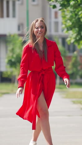 happy young woman in the street. beautiful young lady in passionate red dress is running happily on the city building background. slow motion. vertical video