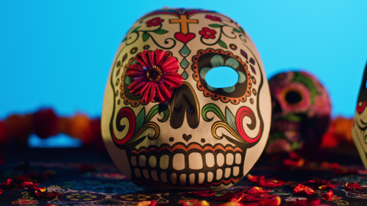 primer plano de cráneos y máscaras decoradas rodeadas de pétalos de flores celebrando la fiesta mexicana de dia de muertos o día de los muertos contra un fondo azul 5