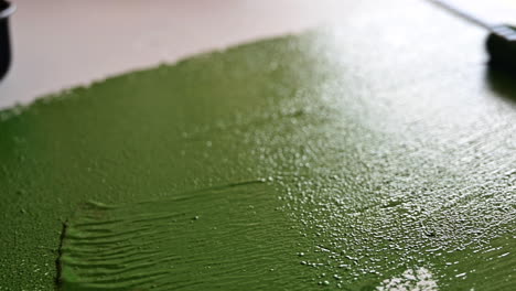 view of man applying green paint to a tabletop during daytime - close up