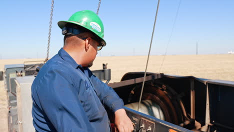 plump man wearing blue uniform and protective helmet stands at the working equipment. worker watches the metal wire is rolled on the rotating cylinder.