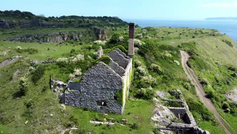 abbandonato ricoperta di edera ricoperta di campagna desolata storica fabbrica di mattoni costiera gallese vista aerea orbita da sinistra a dietro