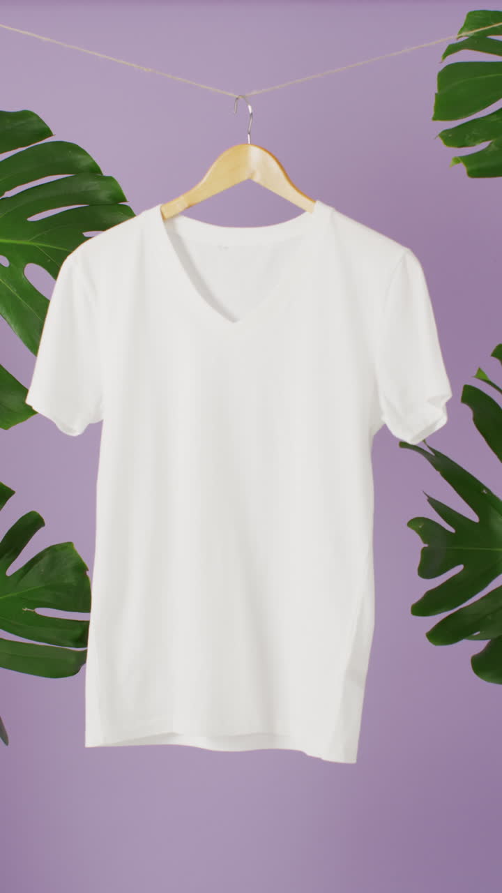 Vertical video of close up of white t shirt hanging on purple background with copy space