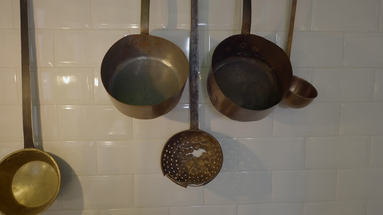 Vintage Copper and Brass Kitchen Utensils Hanging on a White Tile Wall