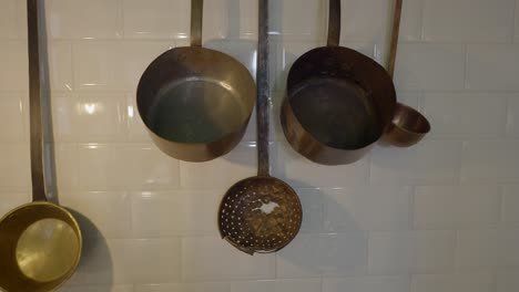 vintage copper and brass kitchen utensils hanging on a white tile wall