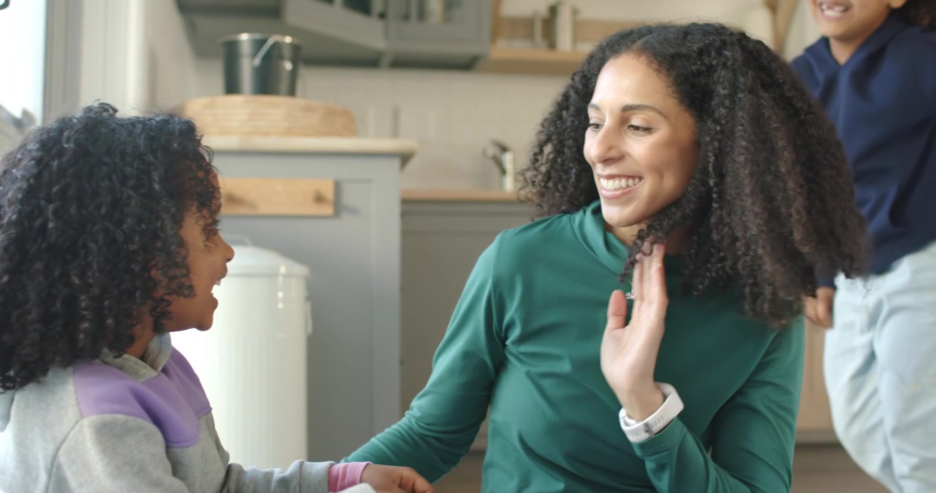 Madre afroamericana che si gira mentre il figlio più piccolo cerca un abbraccio, sistemandosi la felpa in cucina
