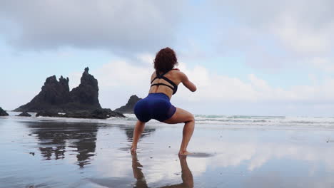 Slow-motion-footage-showcases-a-young,-slim-woman's-training-routine-involving-squats-and-jumps-by-the-ocean's-shore