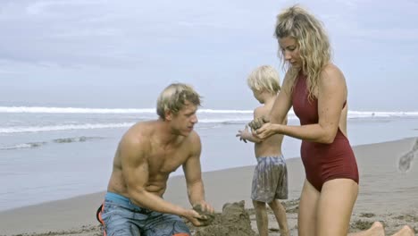 parents and kid tossing wet sand while playing with dog on beach