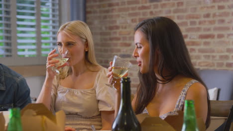 multi-cultural group of friends enjoying drinks and takeaway food at home together