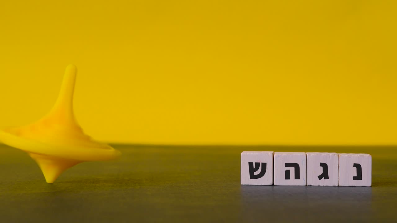 2색 배경에 대한 정적 샷에 표시된 네 개의 히브리어 문자 nun, gimel, heh 및 shin 옆에 회전하는 노란색 상단 하누카 경력