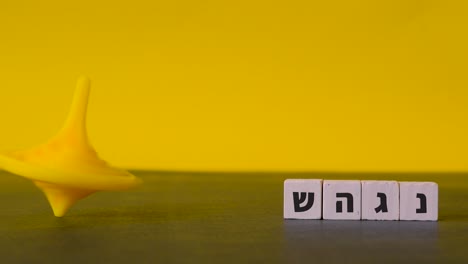 spinning yellow top hanukkah careers about beside the four hebrew letters nun, gimel, heh and shin shown in a static shot against a two-tone background