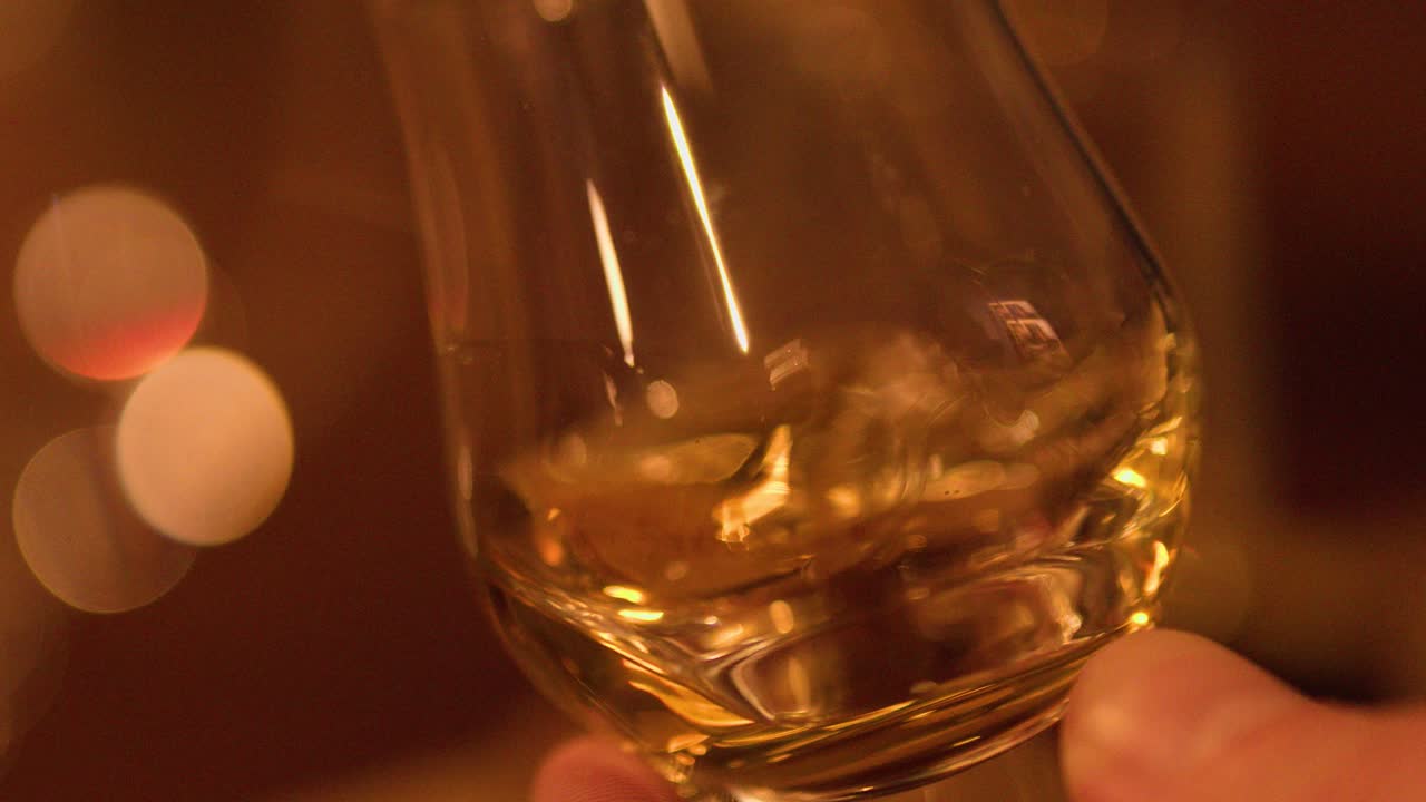 Hand swirls whisky glass in soft, ambient lighting, highlighting golden liquid and elegant reflections