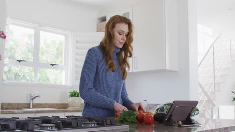 Woman-chopping-fruits-while-using-digital-tablet-in-the-kitchen