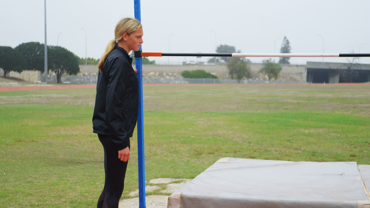 카우카스 여성 운동 선수가 스포츠 장소에서 높은 점프 바를 확인하는 측면 뷰 4k