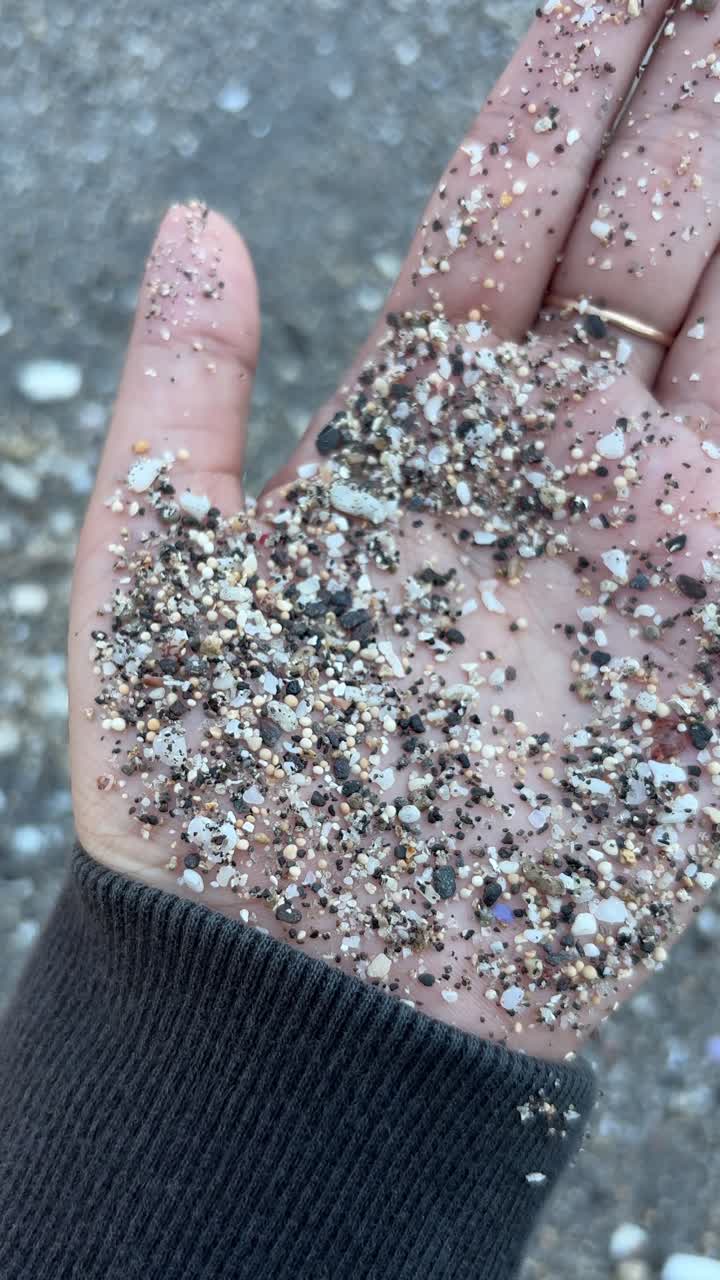 Primer plano de una mano sosteniendo granos de arena mezclados en una playa
