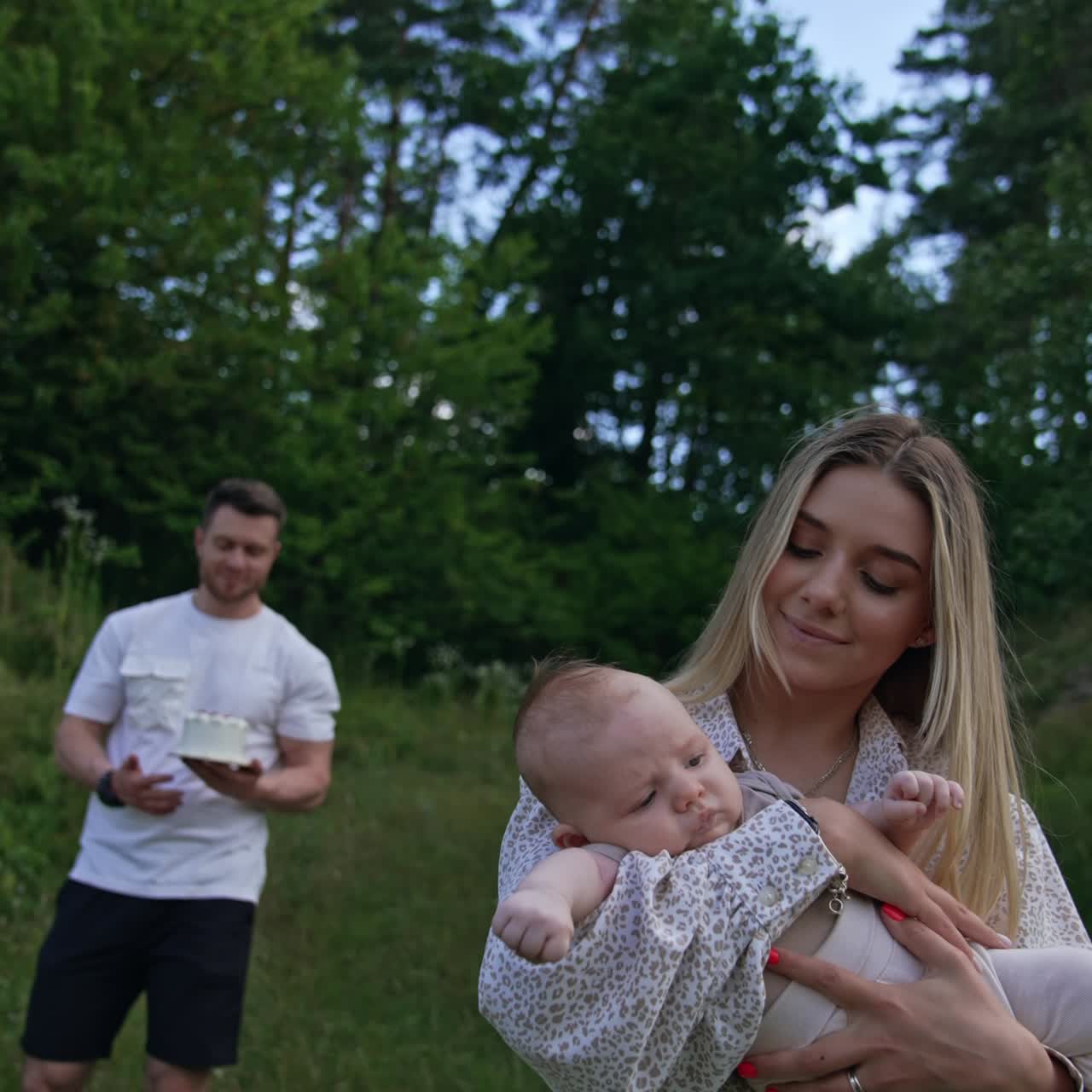 Blonde beautiful woman waving her newborn in hands. Her husband comes up bringing a cake on the plate. Vertical screen