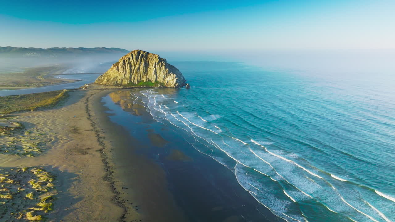 Beautiful white foamy waves coming to the sandy shore with a rock in the middle. Blue waters of Pacific ocean on bright sunny day.