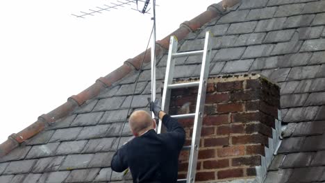 man working on ladder installing digital television aerial on home roof