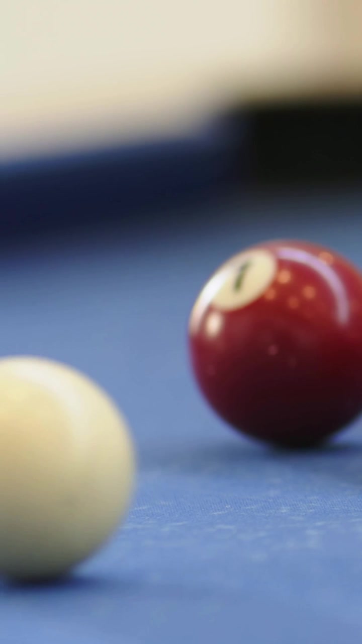 Video verticale: La bilia rossa numero 1 che rotola su un tavolo di feltro blu dopo essere stata colpita dalla bilia bianca, spazio per il testo.