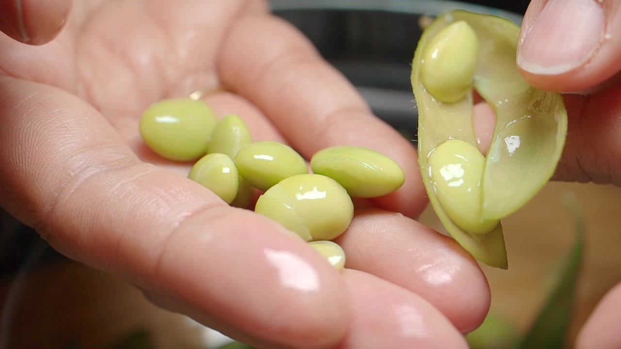 Primo piano di mani che sgusciano fagioli edamame freschi