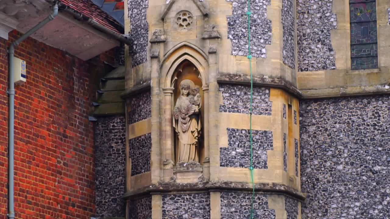 Detailed sculpture of Madonna and Child set in a Gothic niche on a flint and brick church wall in Salisbury, Wiltshire, showcasing British religious architecture.