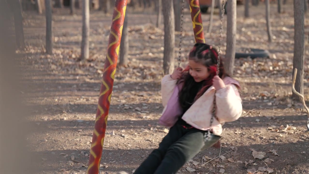 Una giovane ragazza si dondola al rallentatore in un parco giochi boschivo all'aperto, una ripresa cinematografica di lifestyle che evidenzia la gioia dell'infanzia, il movimento giocoso e la ricreazione spensierata tra alberi alti