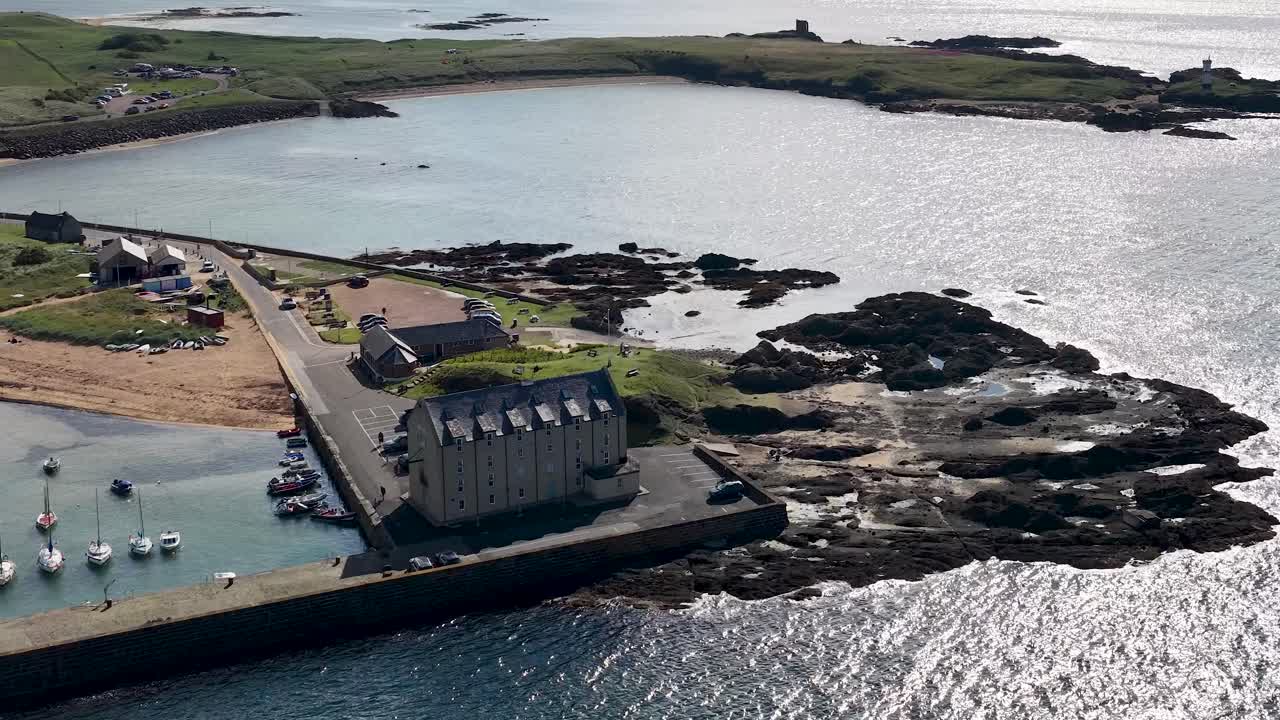 Drone glides above Fife harbor, boats, seaside village, lighthouse ruins, sparkling water, and coastline