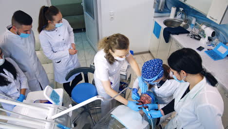 dentistry student having practice on a live patient. group of future dentists stands watching around. top view.