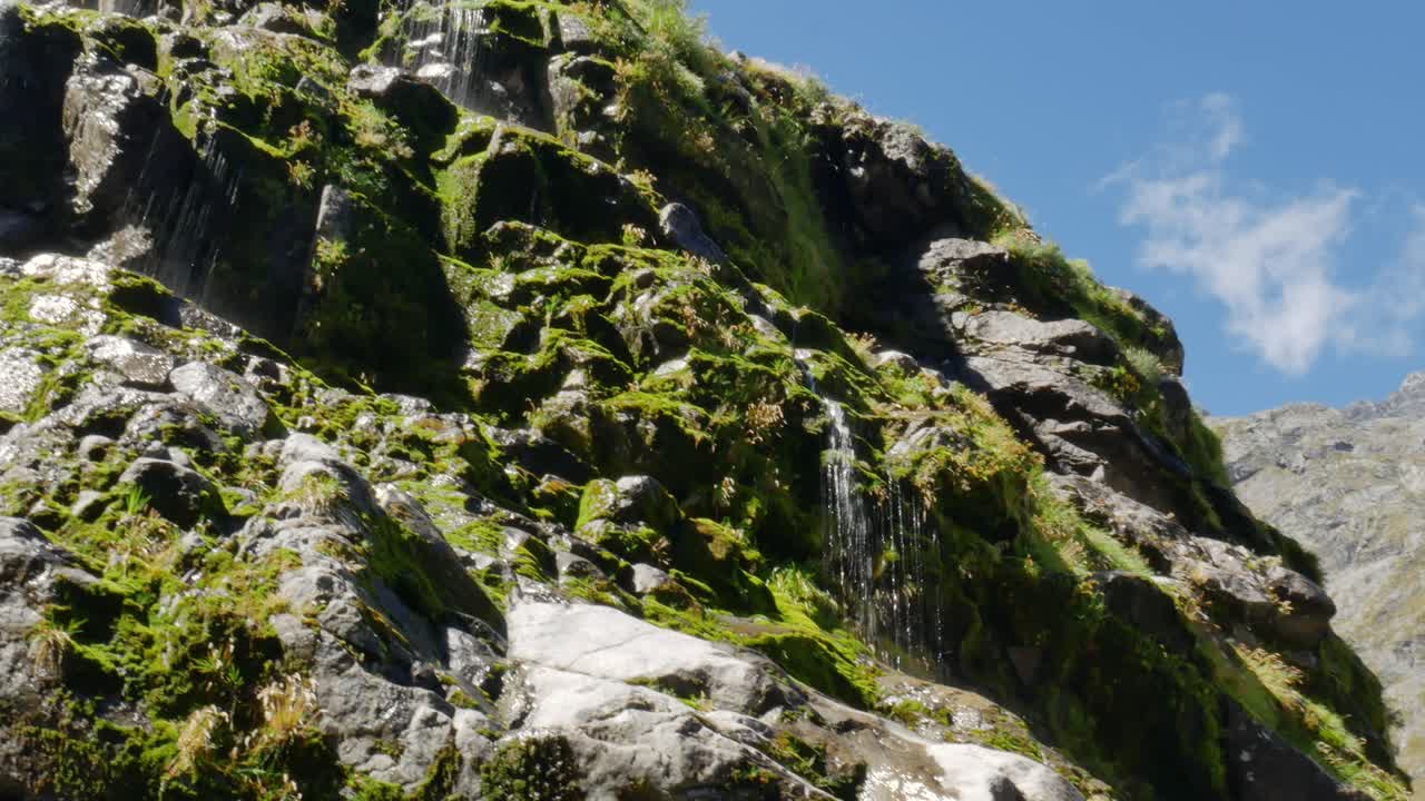 varias pequeñas cascadas que fluyen por las montañas rocosas cubiertas de musgo durante el día soleado en la caminata de la silla de montar gertrude en nueva zelanda