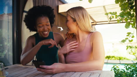 Two Smiling Multi-Cultural Female Friends Outdoors At Home Looking At Mobile Phone