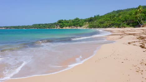 Low-altitude-flight-on-the-beautiful-beach,-Maria-trinidad-Sánchez,-turquoise-blue-water,-fresh-air,-small-waves,-green-vegetation,-on-a-clear-day