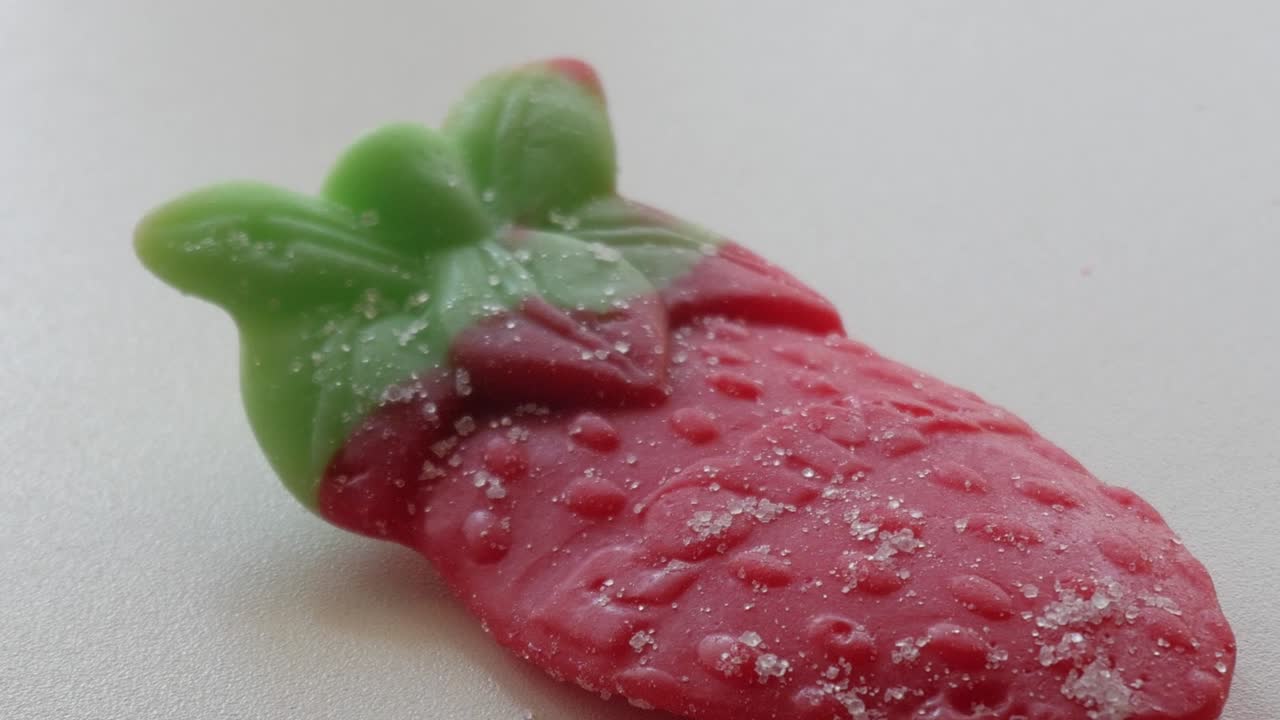 Close-up of a sugared gummy strawberry on a white surface