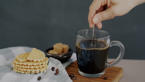 woman stirring coffee with a spoon, waffles and brown sugar cubes on the table