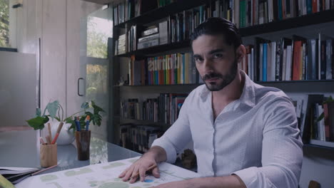 man working on blueprints and looking at the camera ms of latin-american architect working on