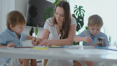 mom helps two sons of 2 and 4 years old to do preschool homework to draw a picture with pencils