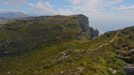 Aerial-shot-flying-over-rugged-nature-on-Table-Mountain-to-reveal-the-city-of-Cape-Town,-South-Africa-in-the-distance-below