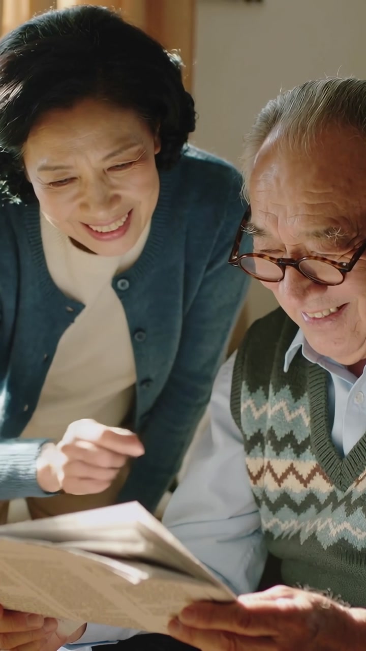 Vertical video: Leaning woman showing paper, man adjusting glasses and reading at home, cardigan