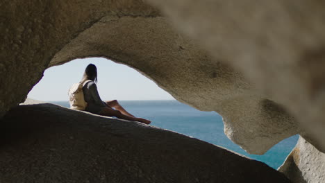 young adventurous woman looking at beautiful ocean view relaxing sitting in seaside cave enjoying peaceful travel vacation alone exploring spiritual freedom