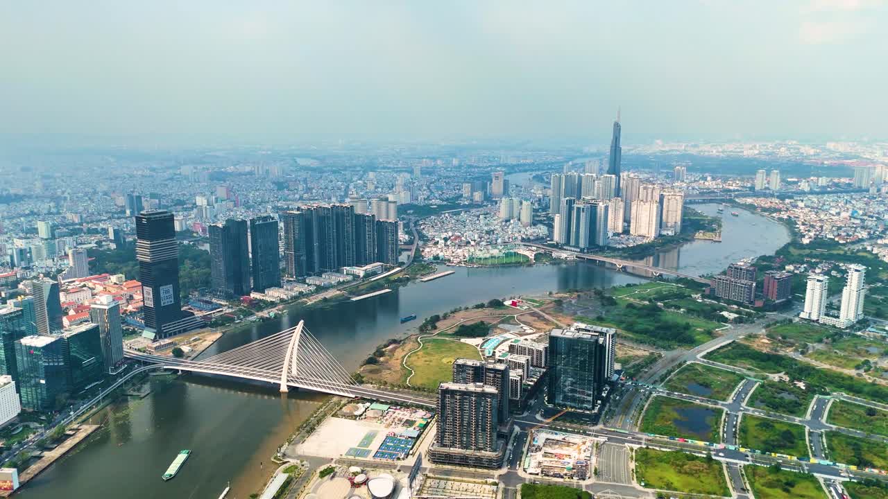 Panoramic aerial view of Ho Chi Minh City skyline with Saigon River, modern skyscrapers, and Landmark 81, Vietnam’s tallest building, under a hazy blue sky.