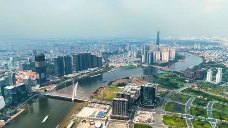 panoramic aerial view of ho chi minh city skyline with saigon river, modern skyscrapers, and landmark 81, vietnam’s tallest building, under a hazy blue sky.