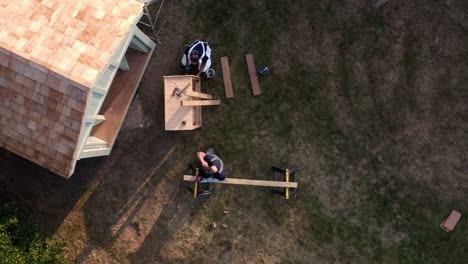 Toma-Aérea-De-Drones-De-Carpinteros-Construyendo-Una-Casa-De-Verano-Al-Aire-Libre-En-El-Jardín.