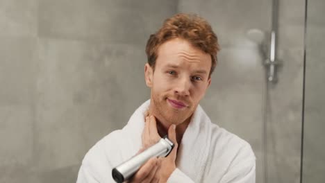 portrait of a handsome man trimming his beard with an electric clipper