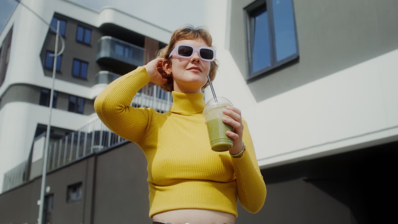 Donna che gusta uno smoothie verde all'aperto in città