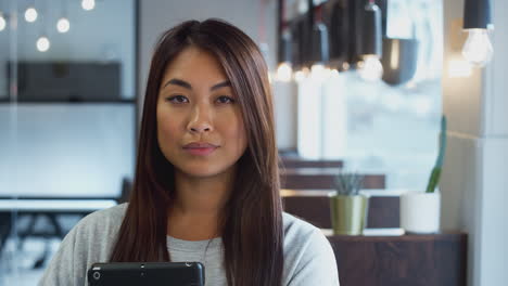 Head-And-Shoulders-Portrait-Of-Smiling-Asian-Businesswoman-Holding-Digital-Tablet-In-Modern-Office