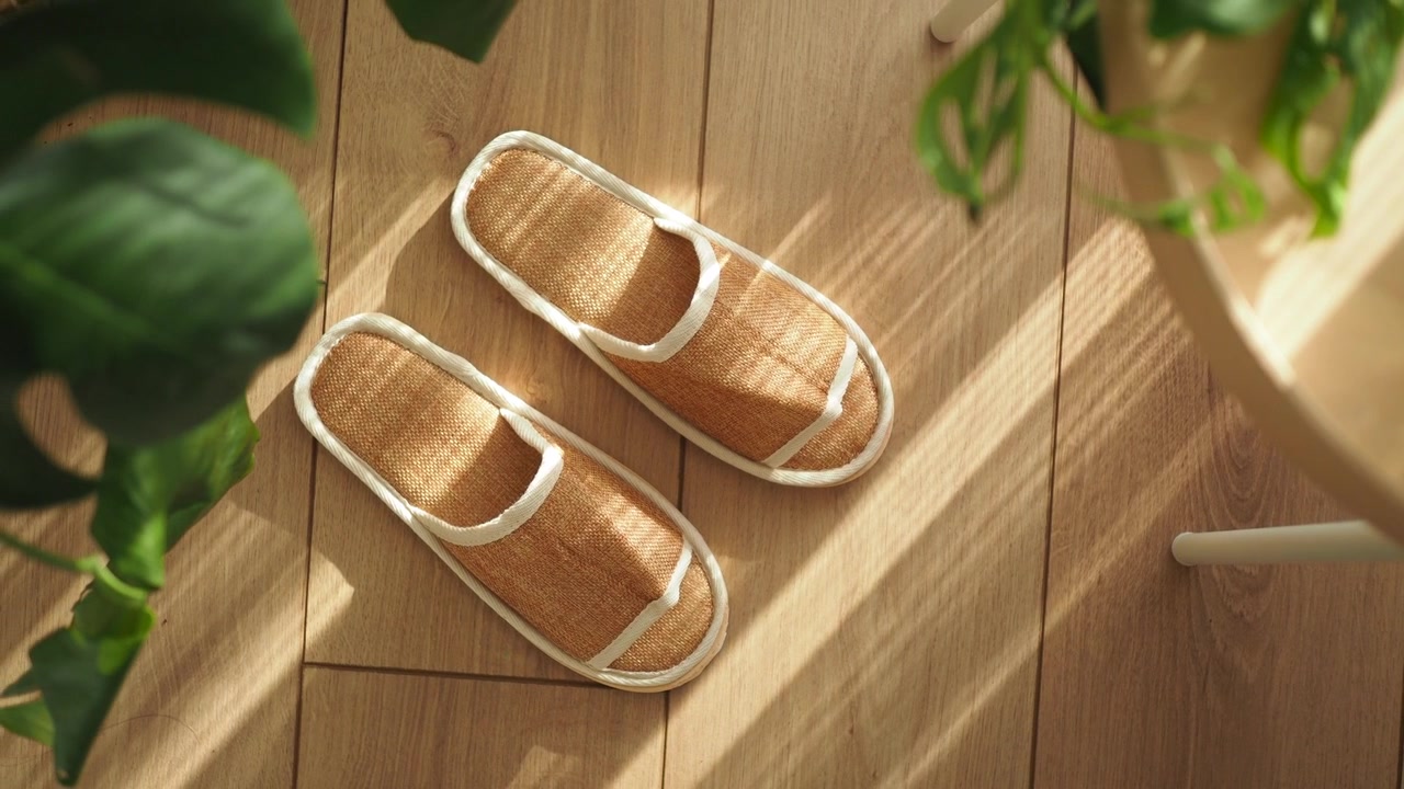 Un paio di pantofole intrecciate su pavimento in legno illuminato dal sole.