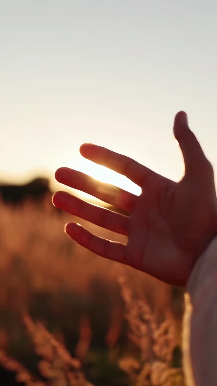 Primo Piano di una Mano che si Allunga verso la Luce Dorata del Sole al Tramonto