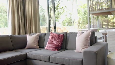 sofá marrón con almohadas, cortinas de oro y ventanas enormes en la sala de estar soleada, cámara lenta