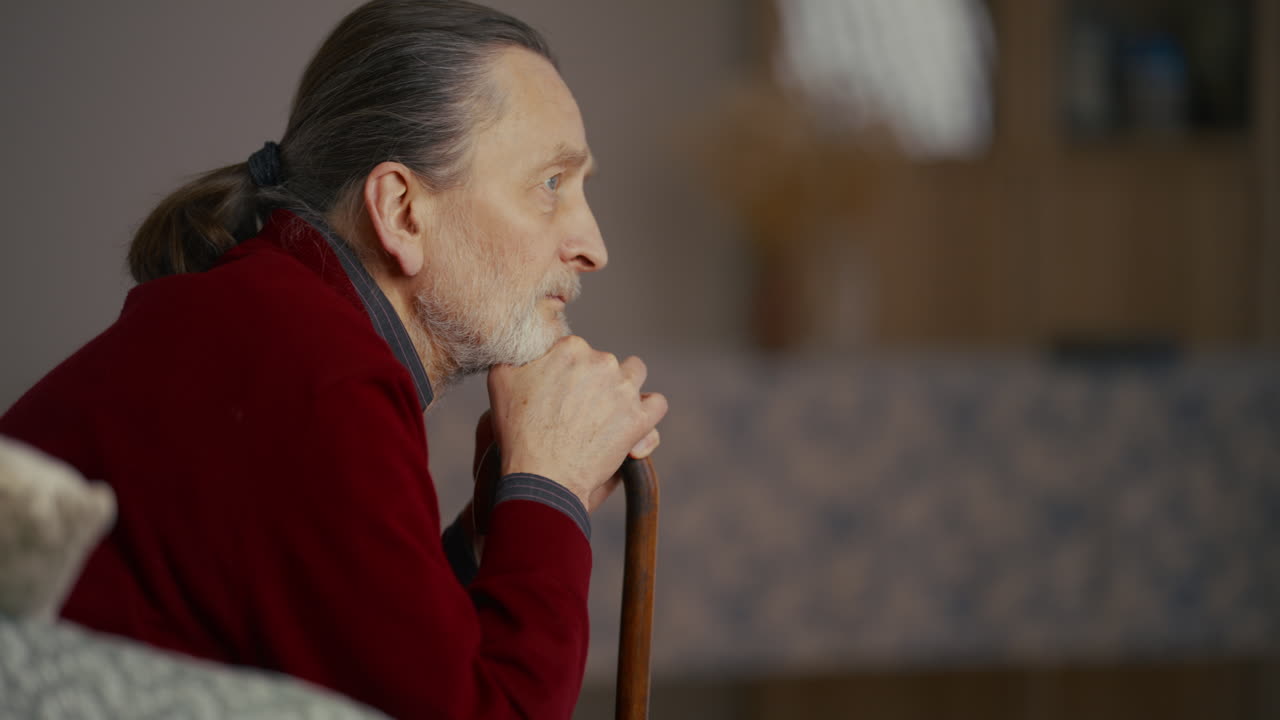 Pensive Elderly Man Sitting with Walking Stick Indoors